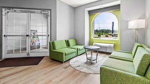 A modern living room with a green sofa set, a small round table, and a large window with a view of greenery. - Quality Inn Shallotte near Ocean Isle Beach (Shallotte)