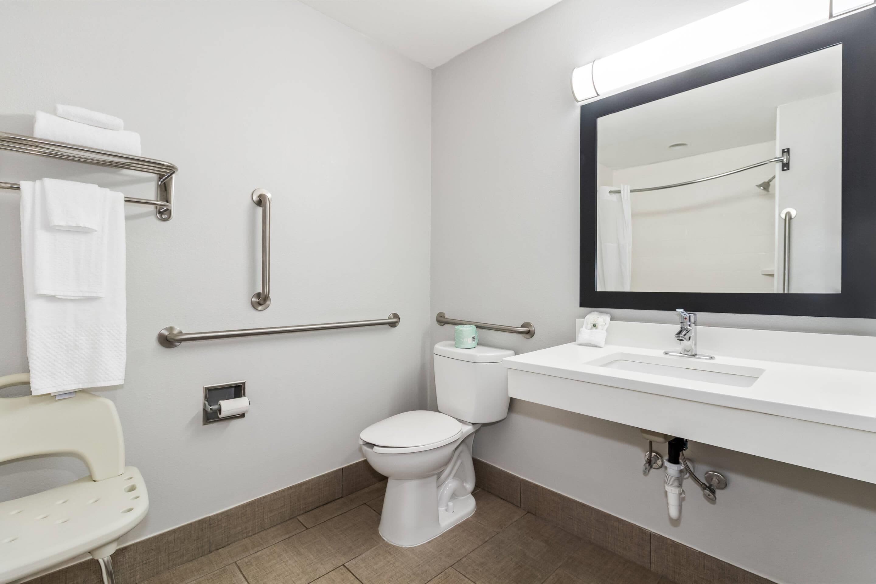 A modern bathroom with a white toilet, a sink with a mirror above it, and a handrail on the wall.