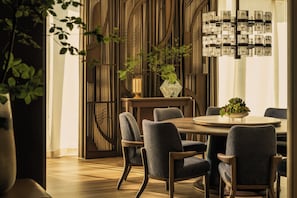A dining area with a round table, six chairs, a vase with plants, and a wall with vertical lines and a chandelier. - Four Seasons Hotel Tokyo at Marunouchi (Tokyo)