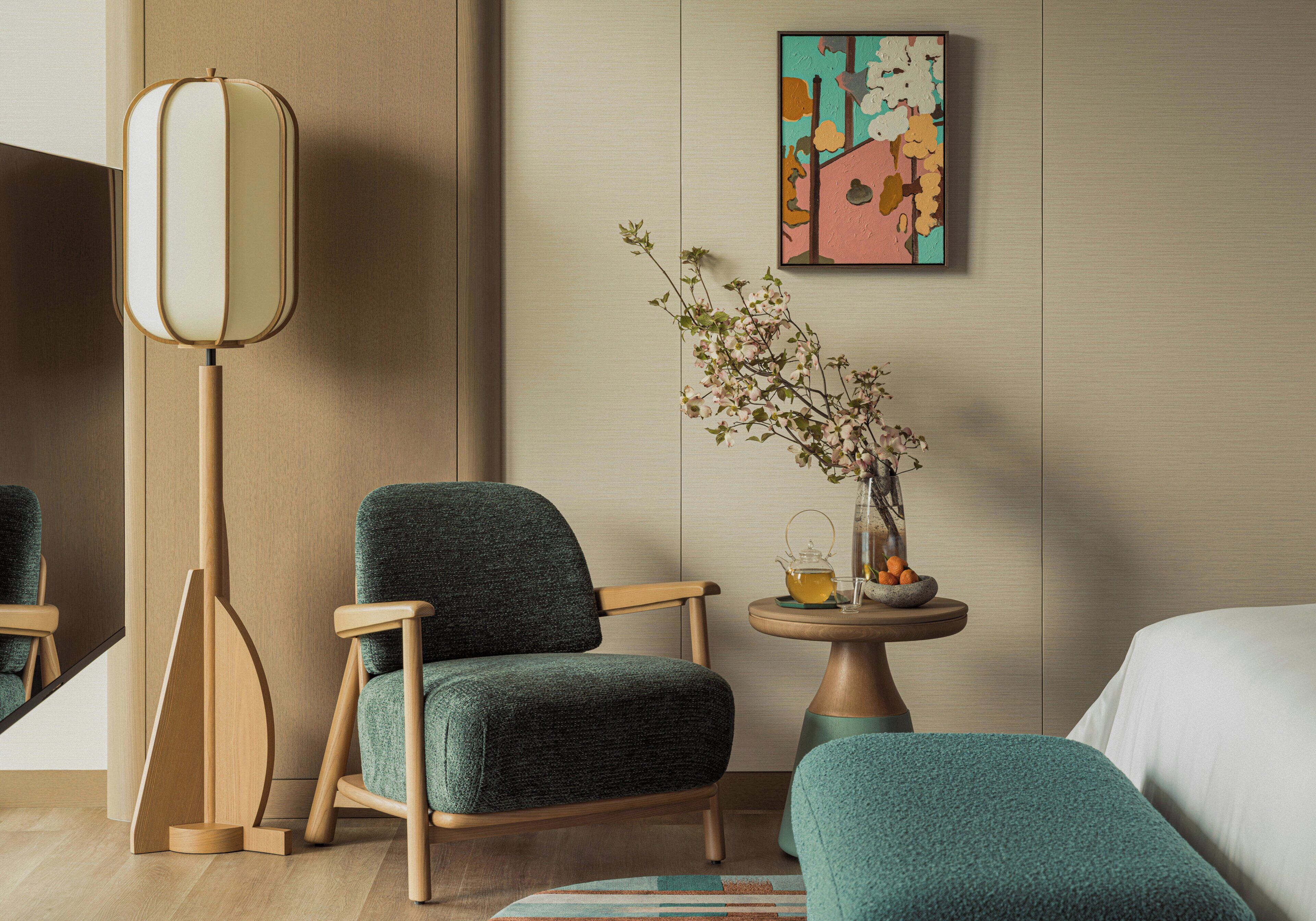 Una habitació d'hotel moderna amb terra de fusta, un butac armchair tapissat de verd, una taula rodona petita amb un ram de flors i un quadre a la paret.