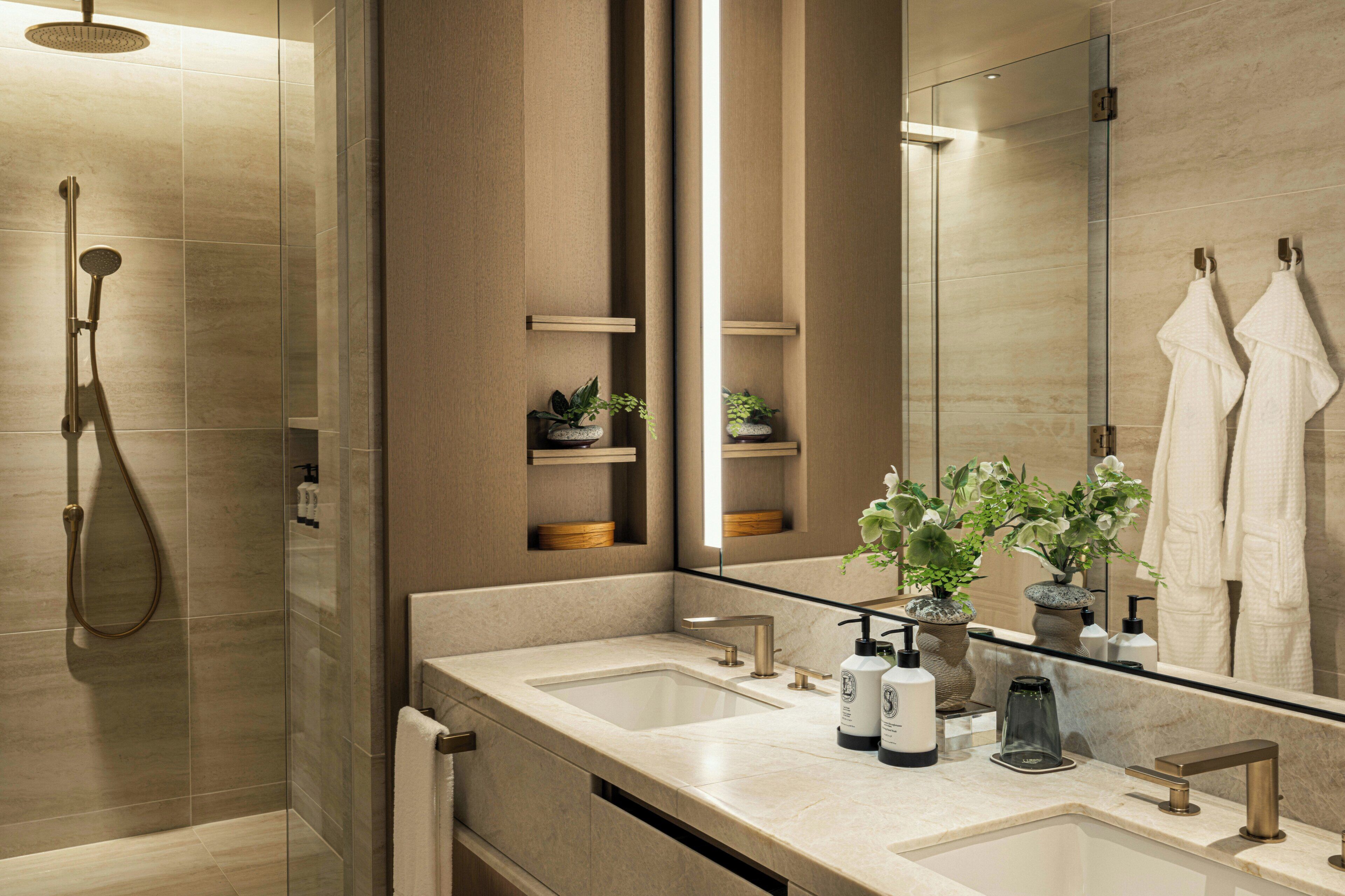 Une salle de bain moderne dotée d’une douche à parois de verre, de deux vasques et d’un grand miroir qui reflète un porte-serviettes.