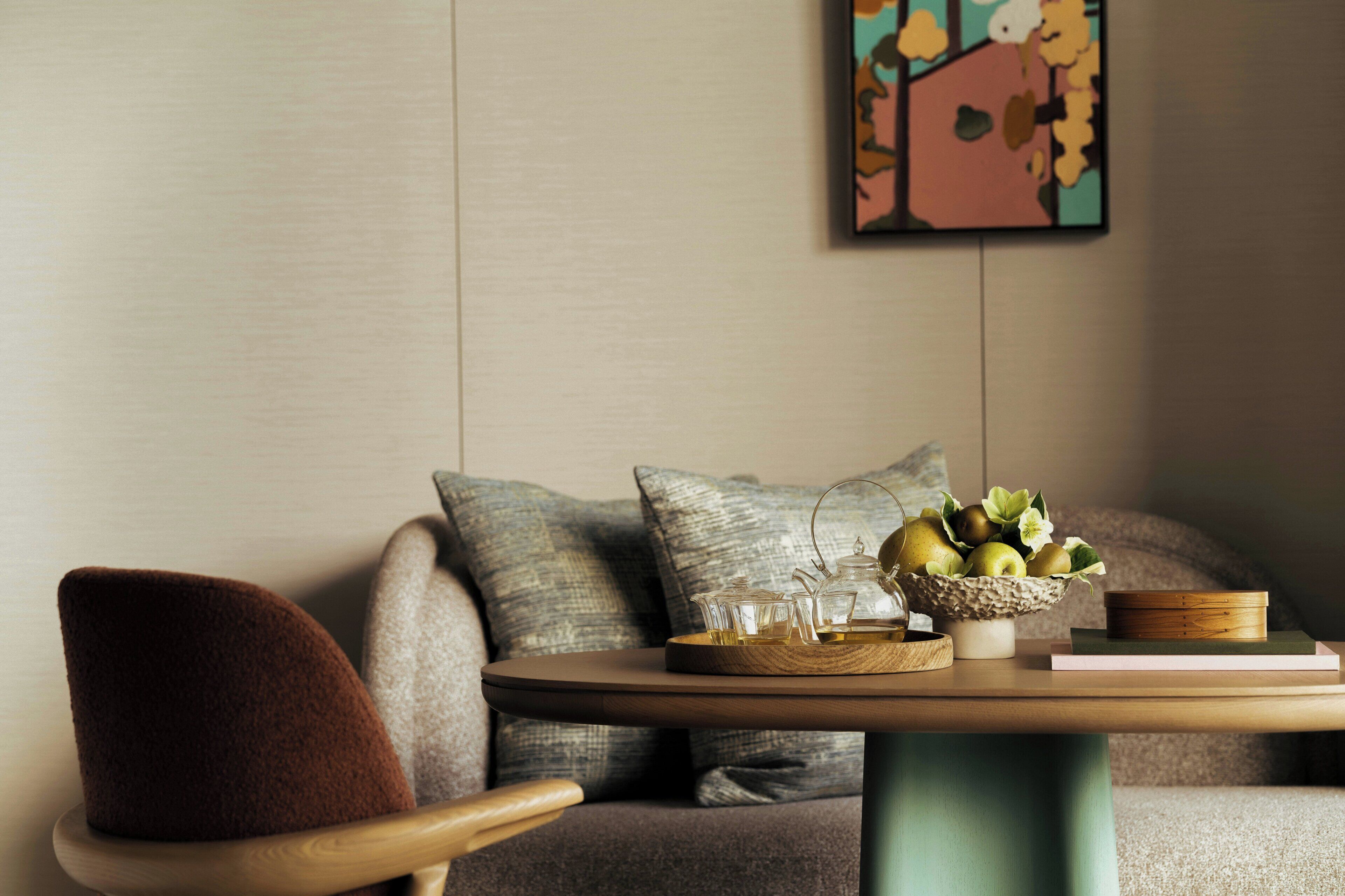 A modern living room with a round wooden table, a sofa with patterned cushions, and a wall-mounted abstract painting.