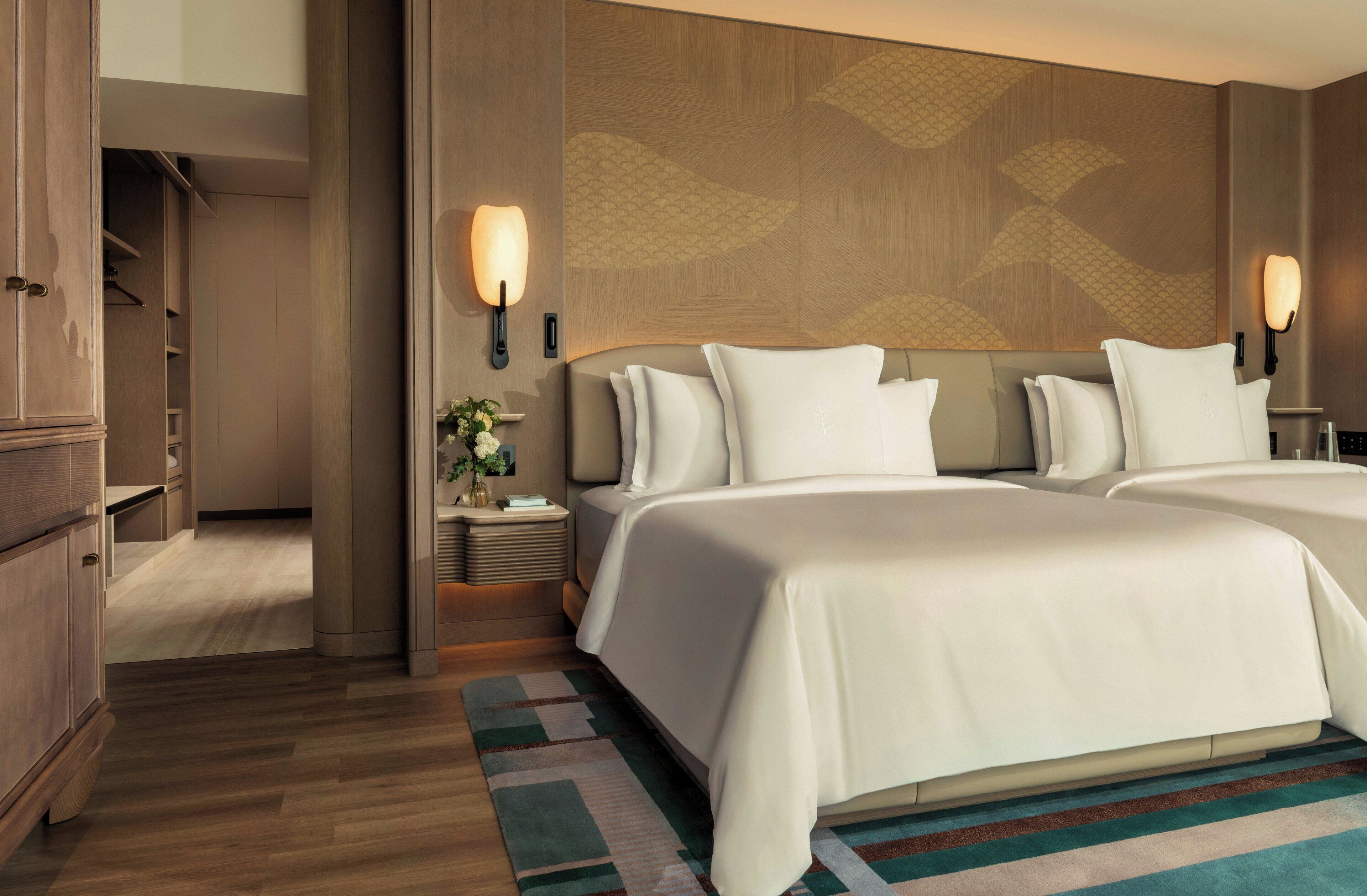 A hotel room with a large bed, a nightstand with a lamp, a wall-mounted light, and a wooden wardrobe.
