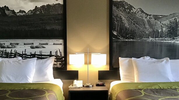 Habitación de hotel con dos camas, una mesita de noche, una lámpara y vistas a montañas y un lago.