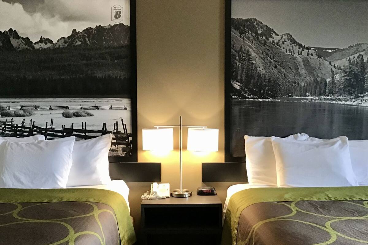 Habitación de hotel con dos camas, una mesita de noche con lámpara y teléfono, y un cuadro grande con un paisaje montañoso.