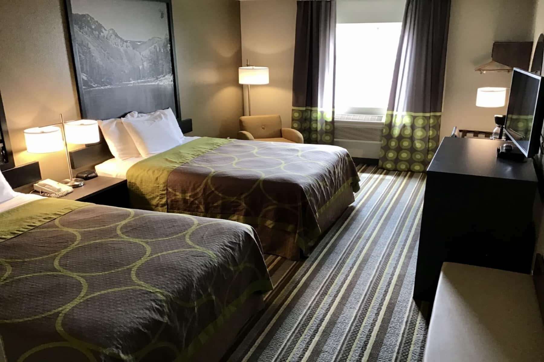 Une chambre d’hôtel avec deux lits, un bureau, une chaise, une télévision et une fenêtre avec des rideaux.