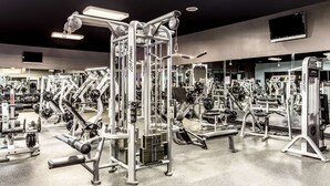 Un gimnasio con diversas máquinas de ejercicio, espejos y equipamiento para levantar pesas.