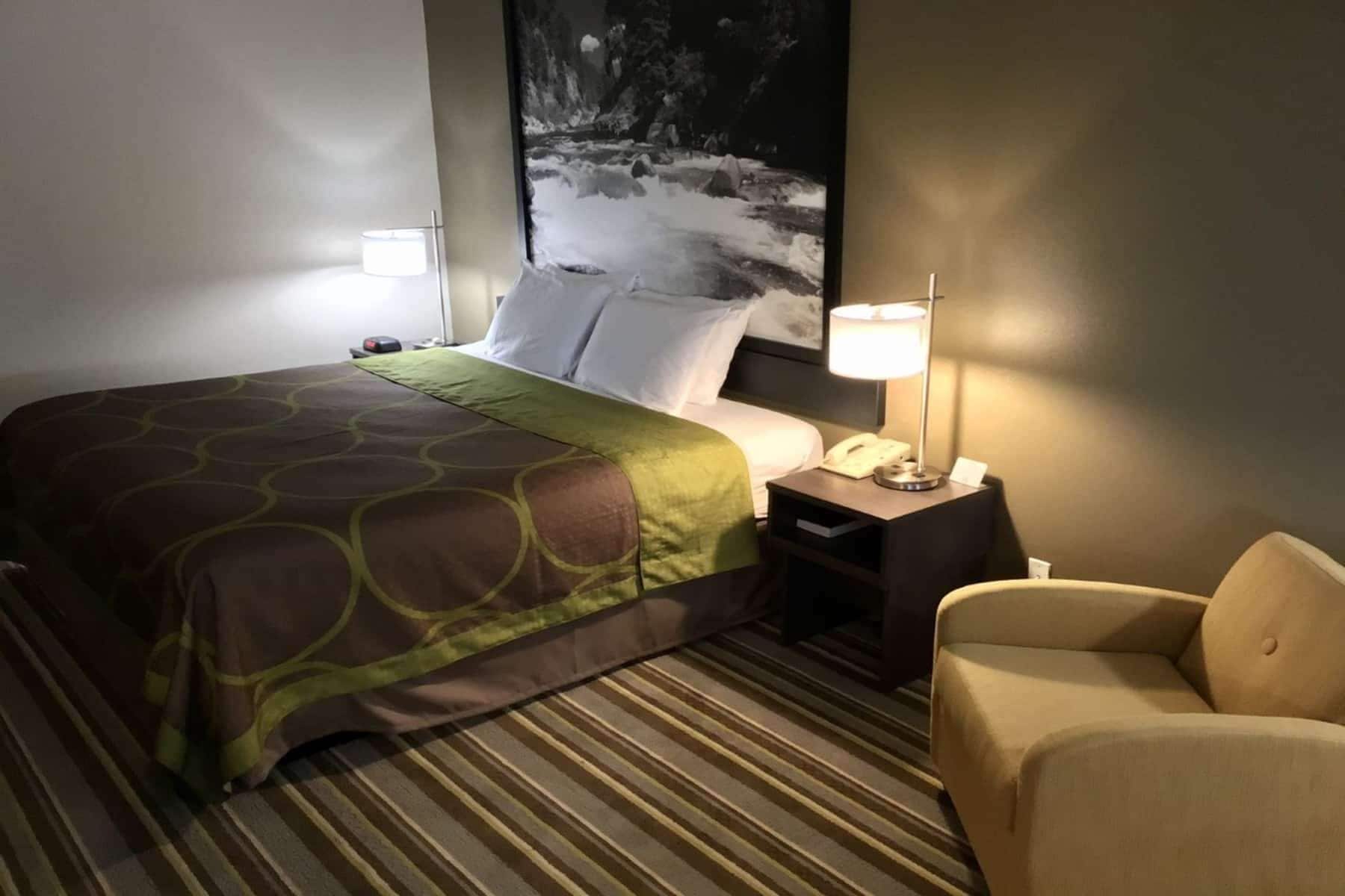 Una habitación de hotel con una cama, una mesita de noche con lámpara, un teléfono y una silla.