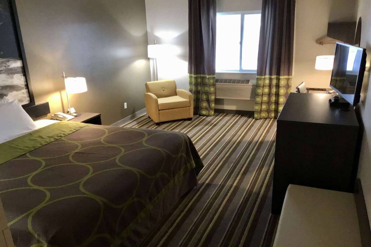 Una habitación de hotel con cama, una silla, un escritorio, un televisor y cortinas.