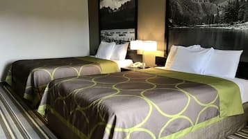 Een hotelkamer met twee bedden, een nachtkastje, een lamp en een groot schilderij van een berglandschap aan de muur.
