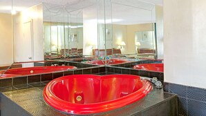 A bathroom with multiple sinks, a large red bathtub, and a mirror reflecting the room. - Knights Inn South Hackensack (South Hackensack)