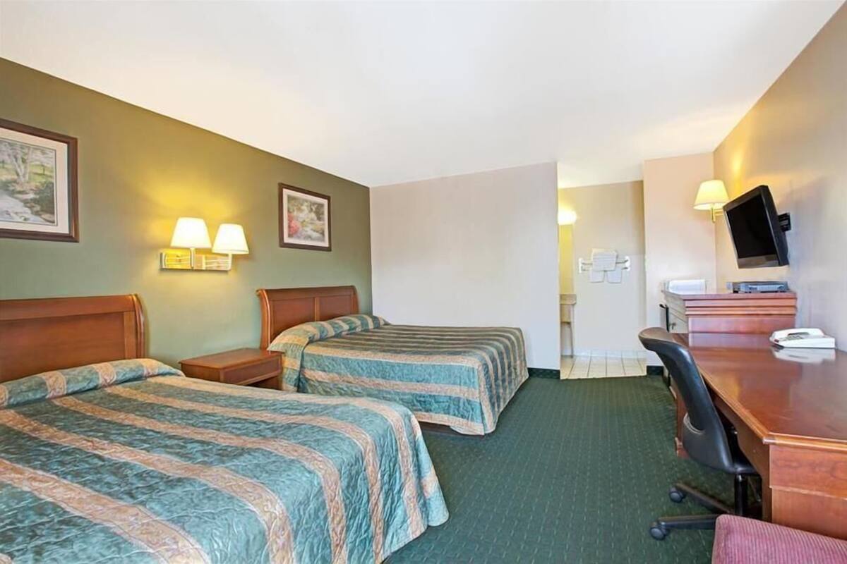 A hotel room with two beds, a desk, a chair, a television, and a bathroom visible through an open door.