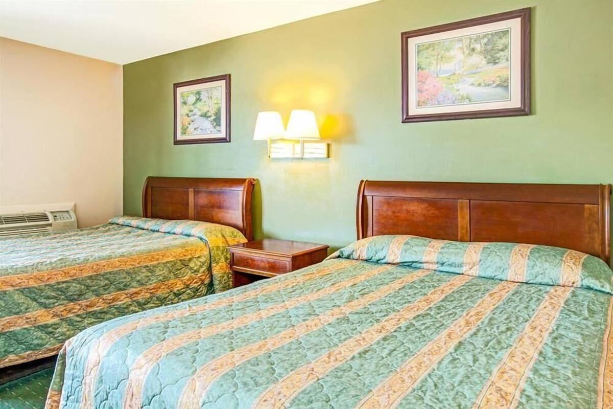 A hotel room with two beds, a nightstand, a wall-mounted lamp, and framed pictures.