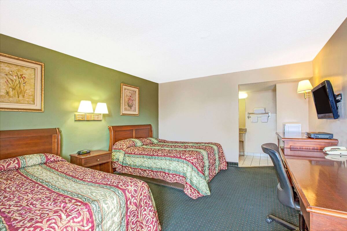 A hotel room with two beds, a desk, a chair, a television, and a bathroom visible through an open door.