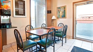 A dining area with tables and chairs, a juice dispenser, a window with a view, and a lamp. - Knights Inn South Hackensack (South Hackensack)