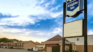 A Knights Inn with a parking lot, a building with a brown roof, and a clear sky. - Knights Inn South Hackensack (South Hackensack)