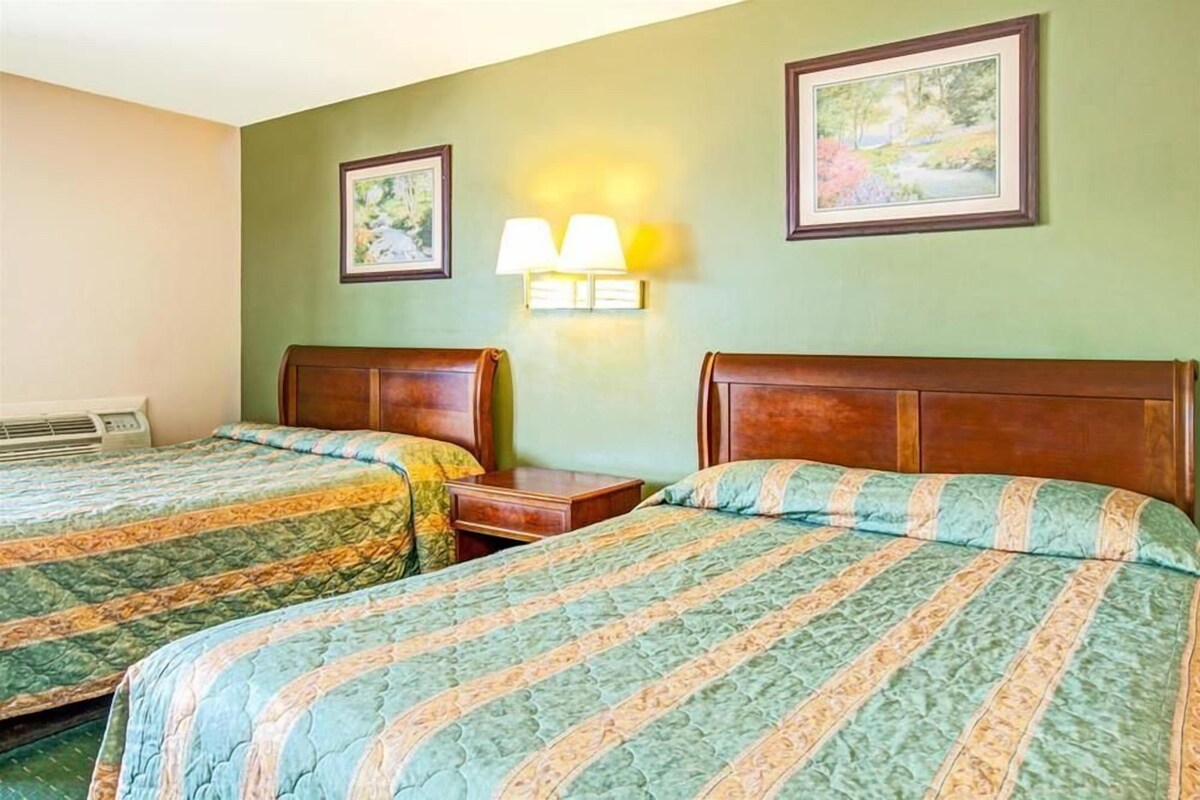 A hotel room with two beds, each with a wooden headboard, a nightstand, and a wall-mounted lamp.