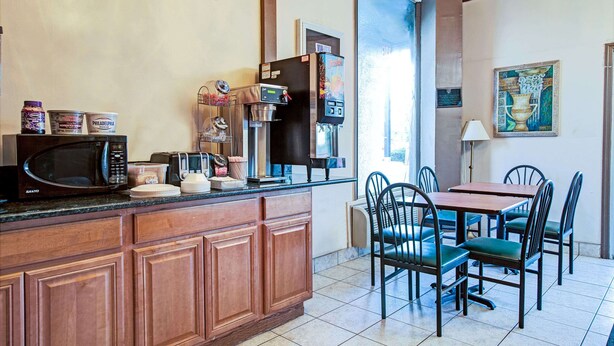 A kitchen with a microwave, coffee maker, and a coffee dispenser. There is a dining table with chairs and a painting on the wall. - Knights Inn South Hackensack (South Hackensack)
