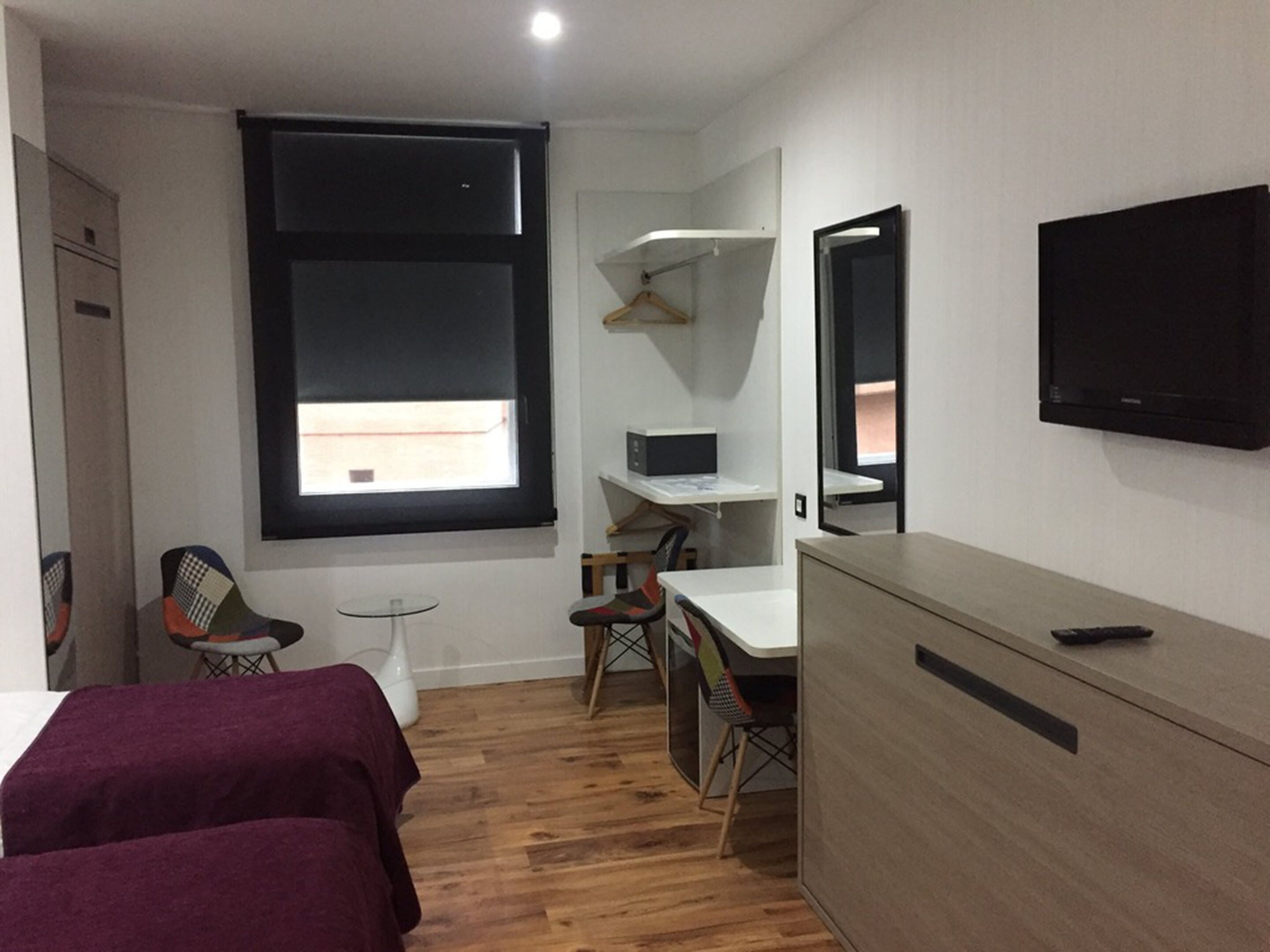 Una habitación de hotel compacta con cama, escritorio, silla, televisión y ventana.