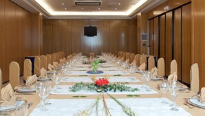 Une salle de conférence dotée d’une longue table préparée pour un événement formel, et équipée de chaises, de tables et d’un téléviseur à écran plat.