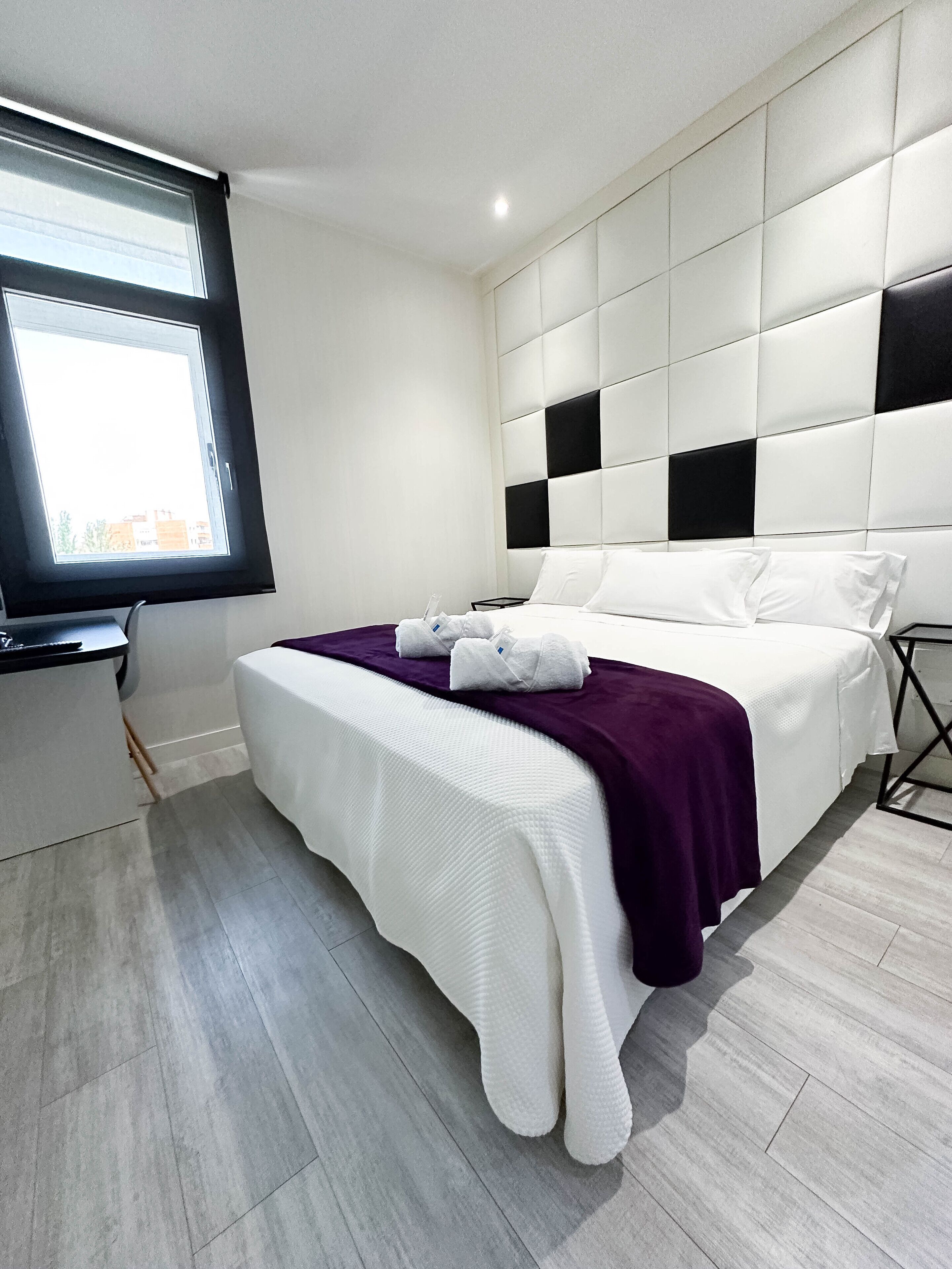 A modern hotel room with a large bed, a window, and a flat-screen TV.