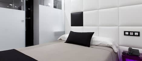 Un dormitorio moderno con una cama grande, una mesita de noche con un teléfono y una lámpara fijada a la pared.