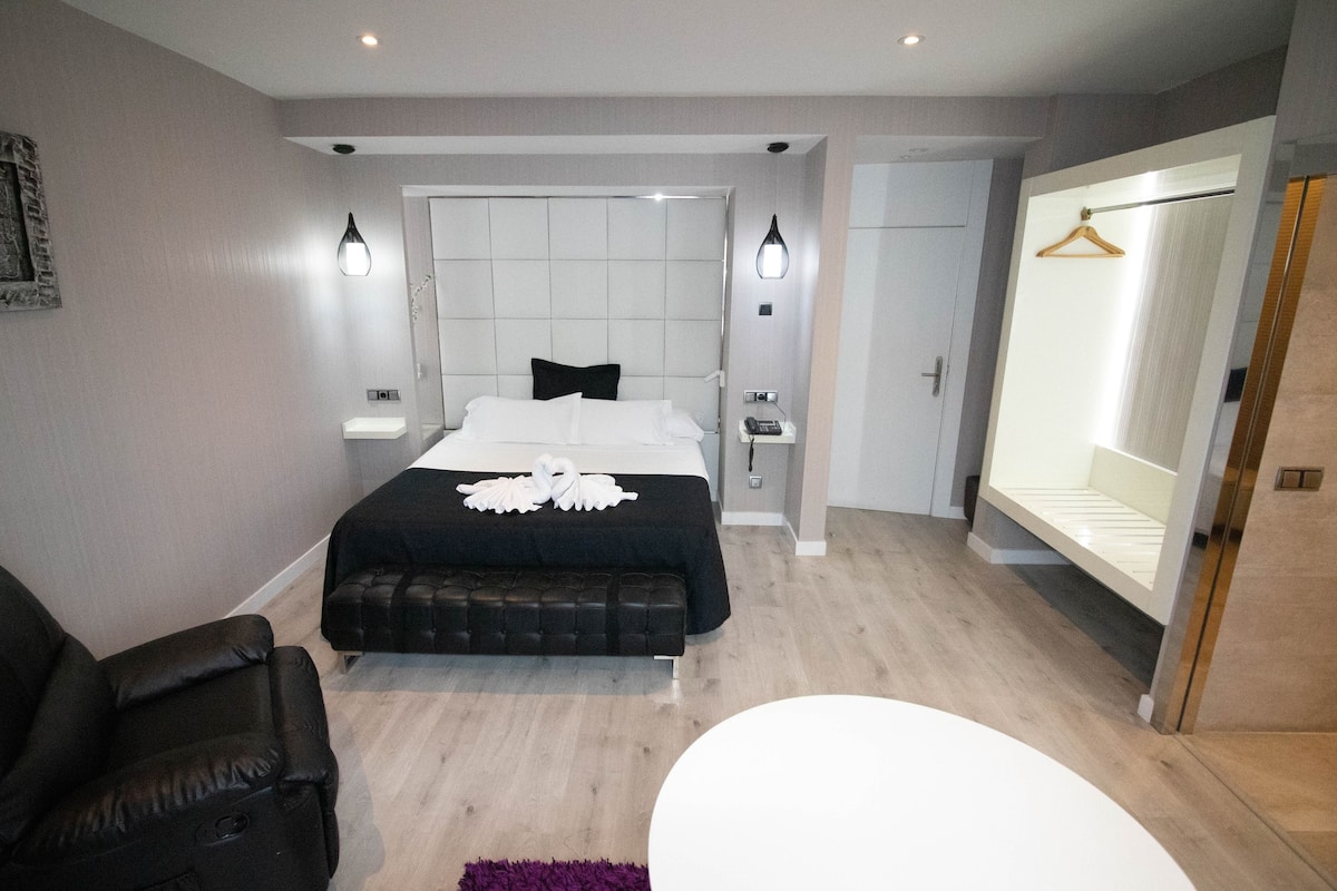 Een moderne slaapkamer met een bed, nachtkastjes, een stoel en een grote spiegel.