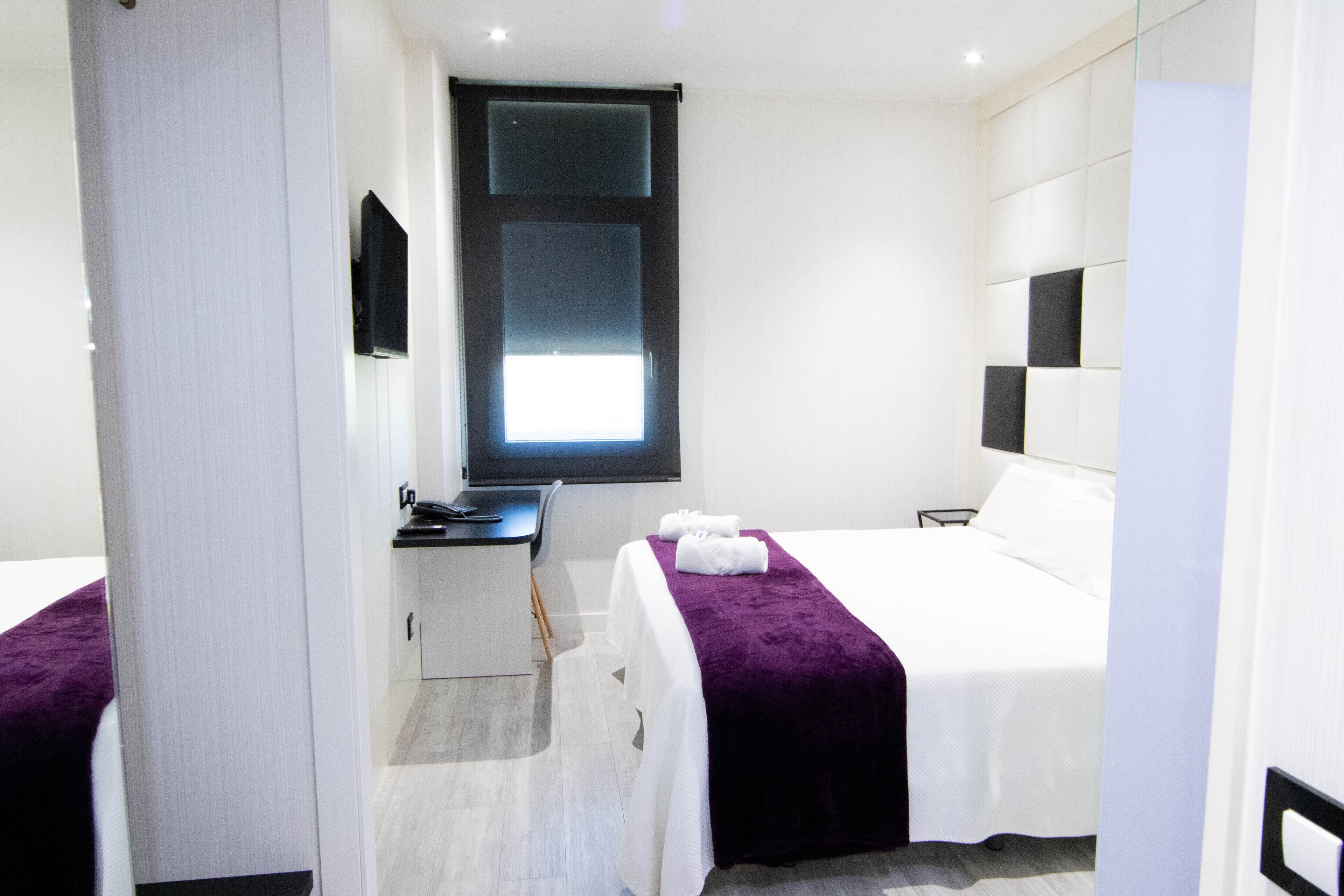 Une chambre d’hôtel moderne, équipée d’un lit, d’un bureau et d’une fenêtre.