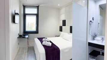 Une chambre d’hôtel moderne équipée d’un lit, d’un bureau, d’une grande fenêtre, d’une salle de bain avec un miroir et d’un porte-serviettes.