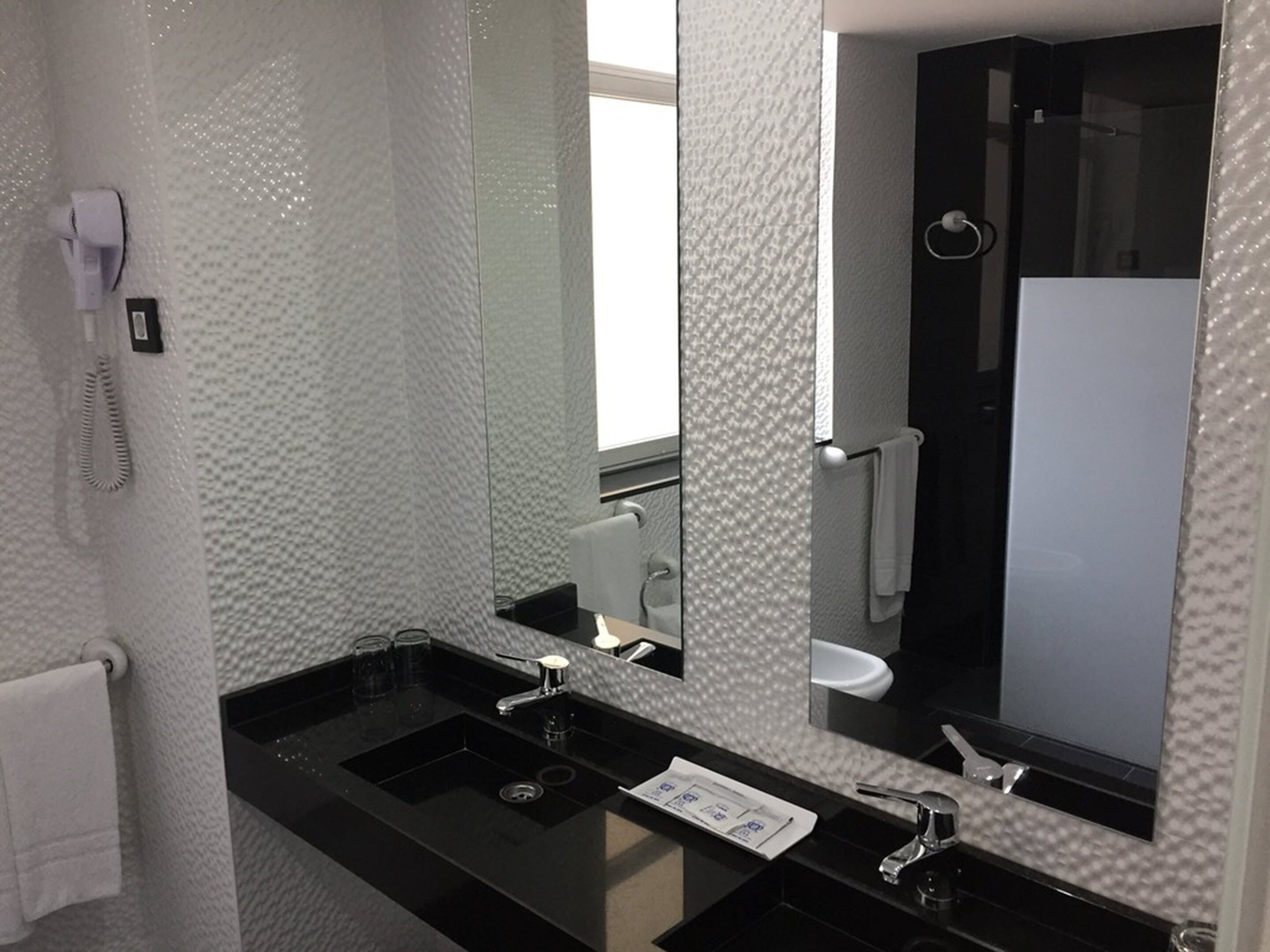 Un baño moderno con un lavamanos negro, un espejo grande y una zona de ducha.