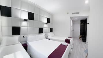 Habitación de hotel con diseño moderno, que incluye una cama grande con ropa de cama blanca y un plaid morado, dos camas más pequeñas, una pared a cuadros y un pasillo que lleva a un baño.