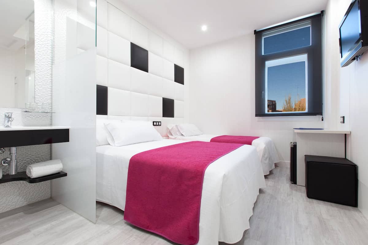 Een moderne hotelkamer met twee bedden, een groot raam, een televisie en een badkamer met spiegel en wastafel.