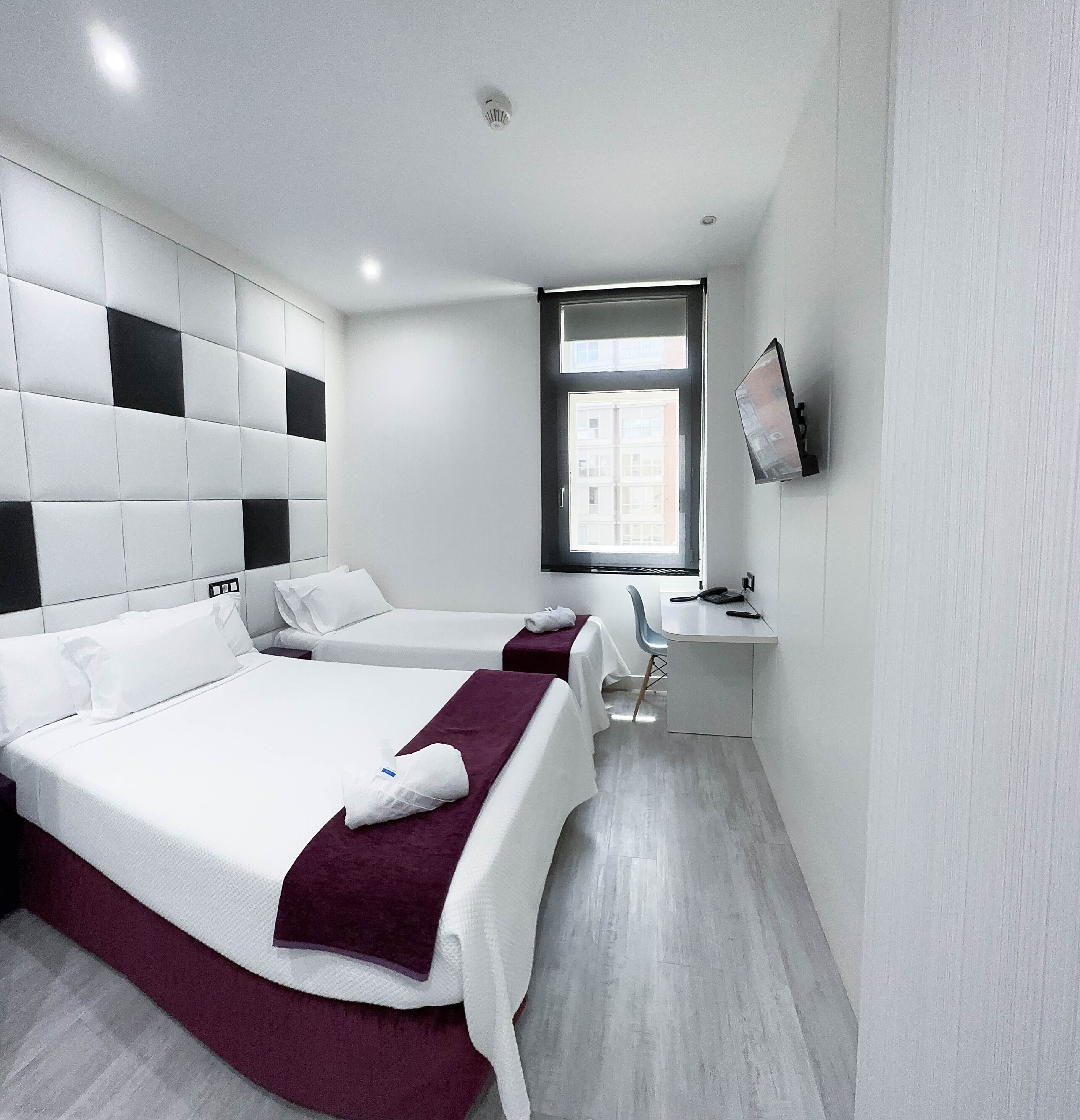 Una habitación de hotel moderna con una cama grande, otra más pequeña, un escritorio y un televisor en la pared.