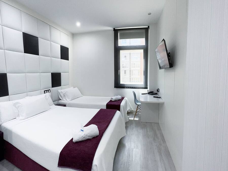 Una habitación de hotel moderna con una cama grande, otra más pequeña, un escritorio y un televisor en la pared.