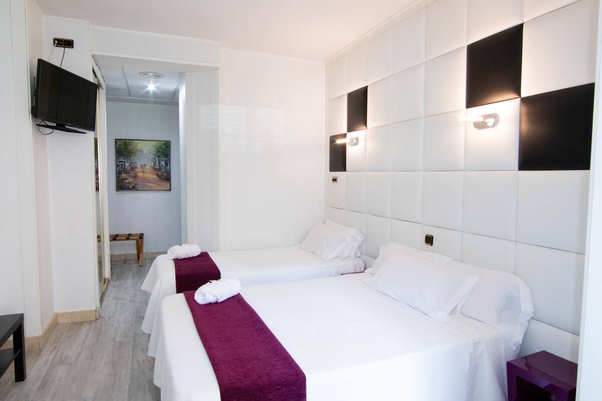 Een hotelkamer met twee bedden, een aan de muur bevestigde televisie en een schilderij op de deur.