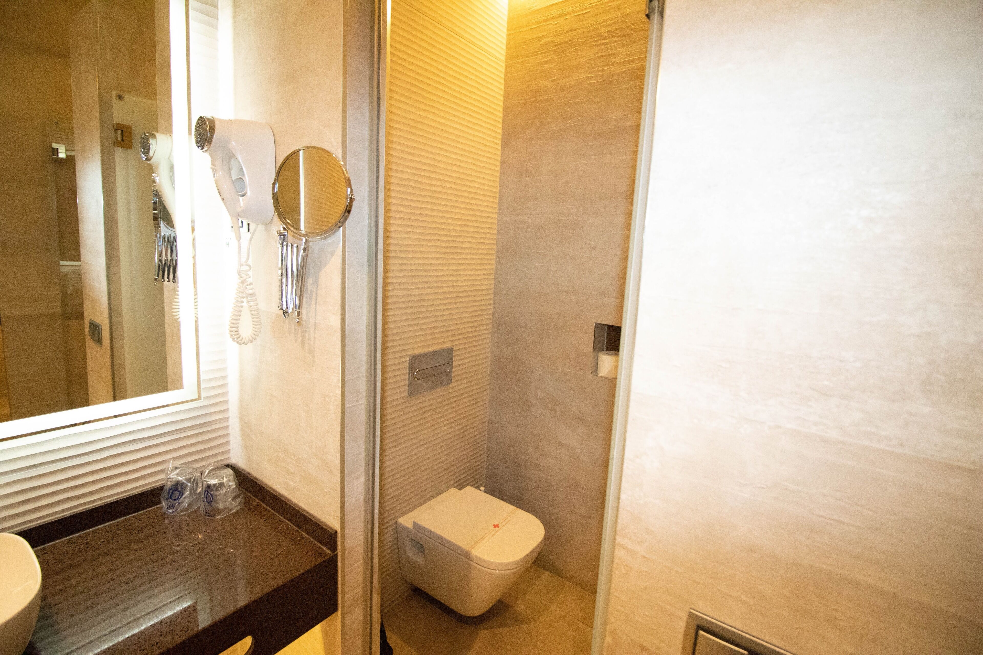 Casa de banho com sanita, lavatório, espelho e secador de cabelo.