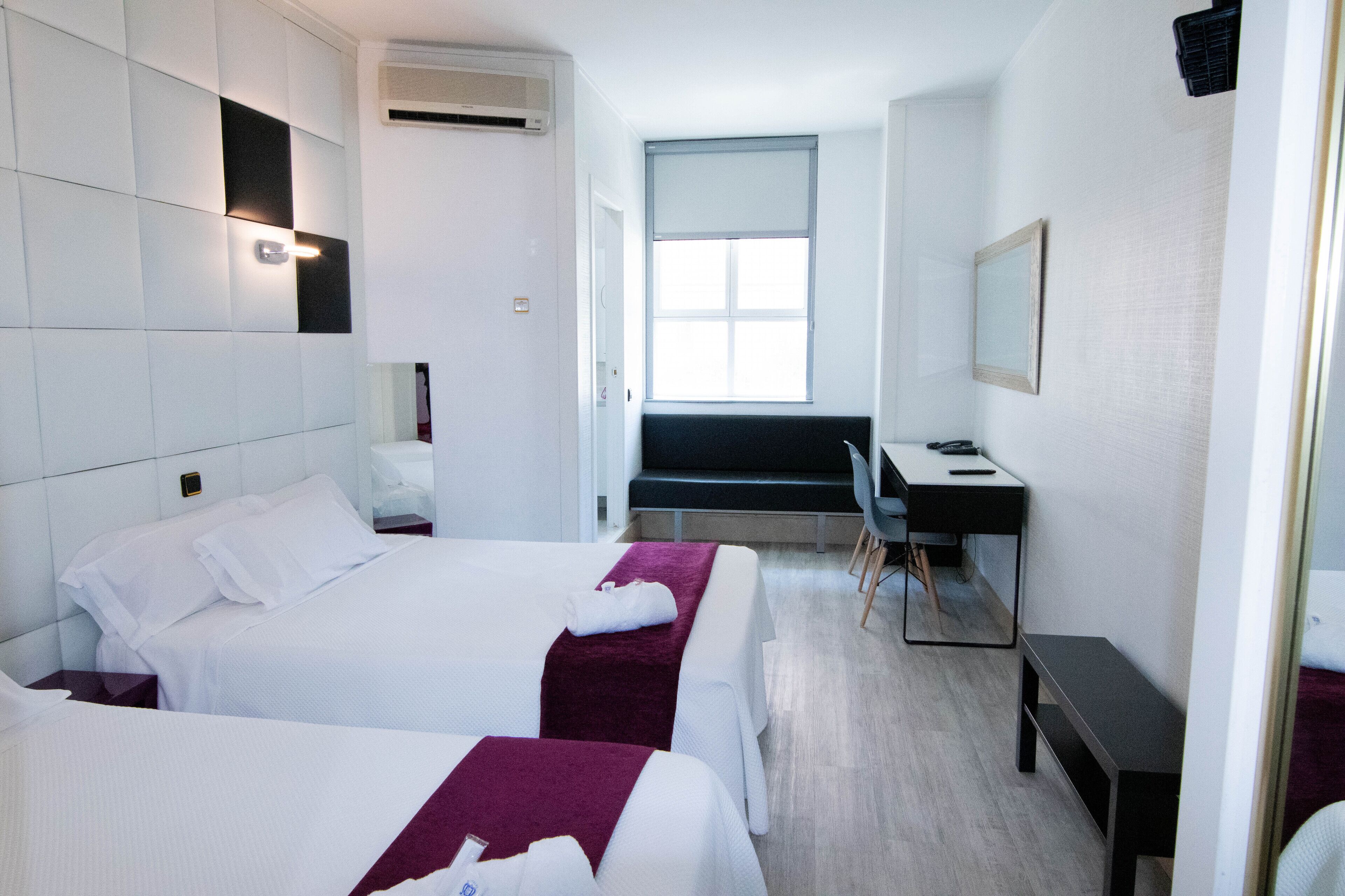 A hotel room with two beds, a desk, a chair, and a large window.