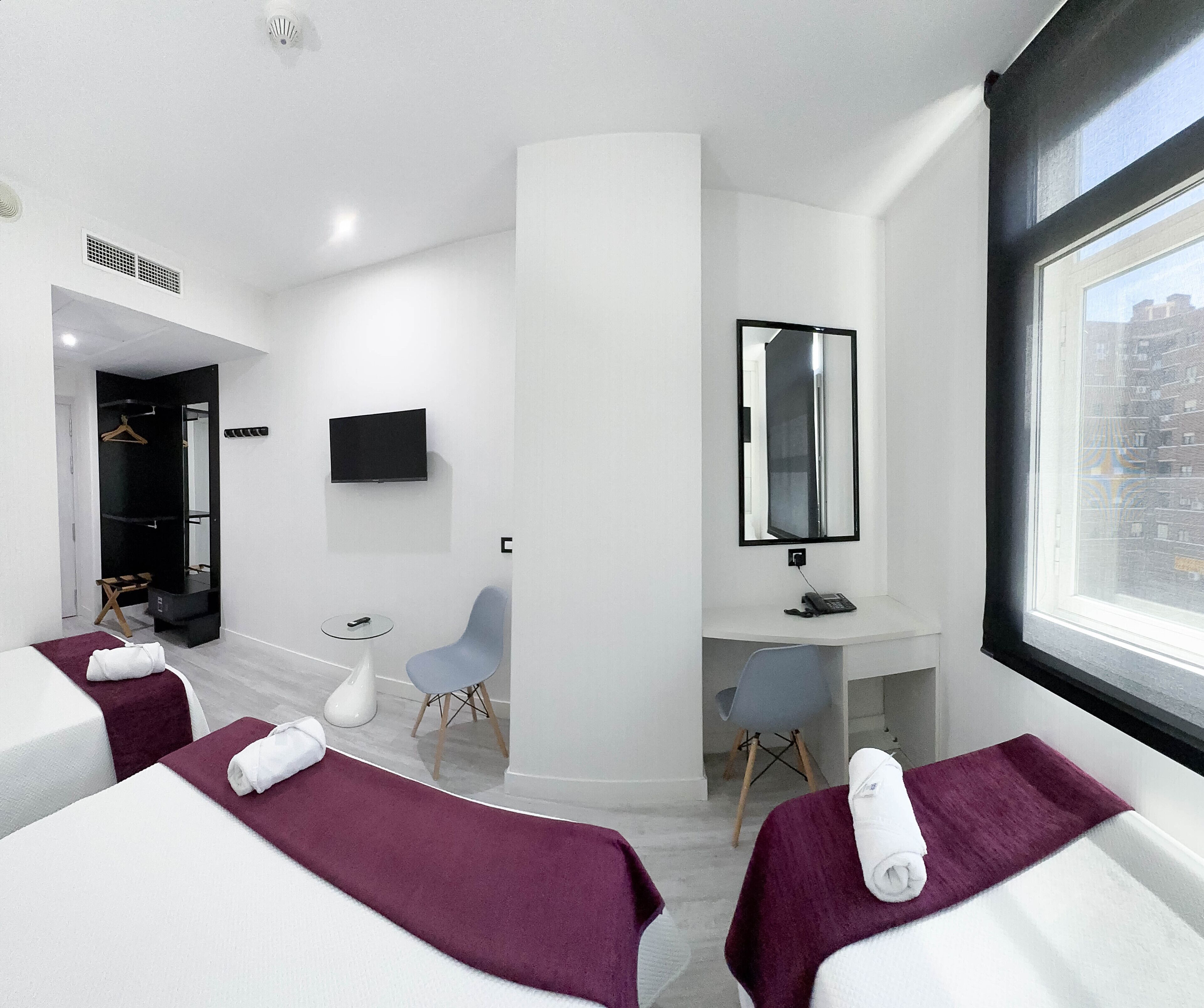 A modern hotel room with two beds, a desk, a chair, a TV, and a large window.