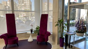Un hall d’entrée avec deux fauteuils violets, un vase blanc contenant une orchidée et une table en verre.