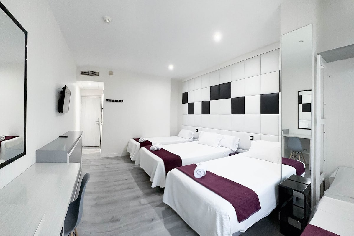 Een hotelkamer met drie bedden, een bureau en een spiegel.