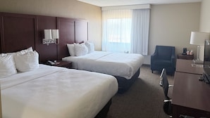 A hotel room with two beds, a desk, a chair, a lamp, and a window with curtains.