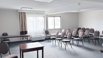 Konferenssihuone, jossa on pitkä pöytä, useita tuoleja, ikkuna, jossa on verhot, ja kattovalaisin.