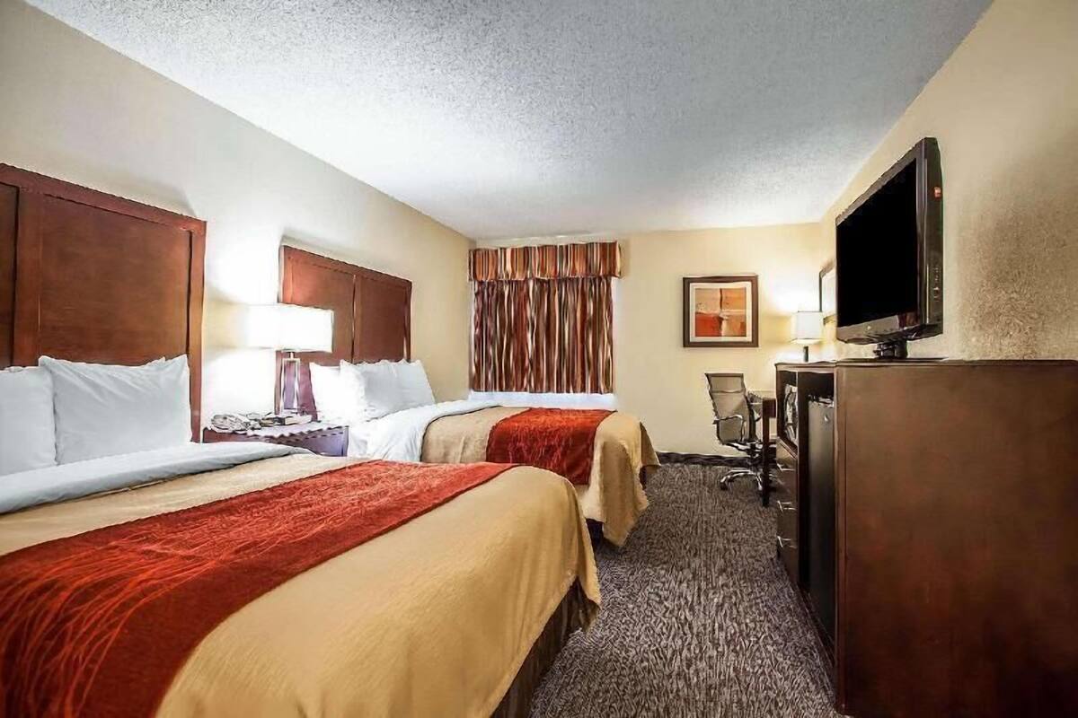 A hotel room with two beds, a desk, a television, and a chair.