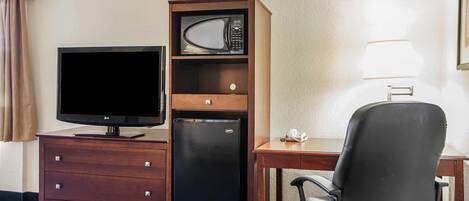 A hotel room with a flat-screen TV, a microwave, a refrigerator, a desk, and a chair.