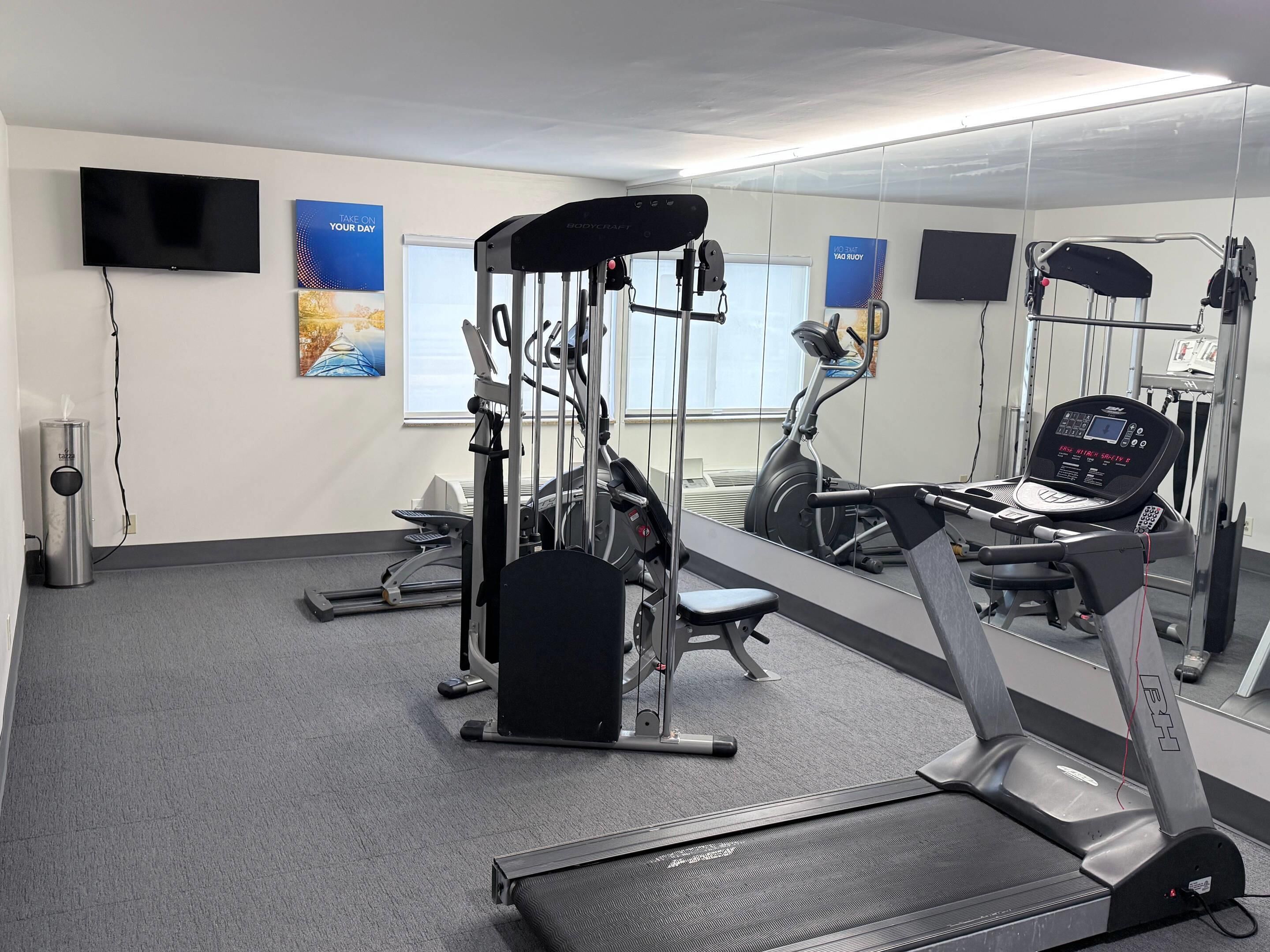 Et fitnessrum med løbebånd, træningsmaskiner og spejle på væggene.