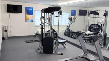 Et fitnessrum med løbebånd, træningsmaskiner og spejle på væggene.