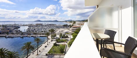 A balcony with wicker furniture overlooking a marina with boats and a cityscape in the background.