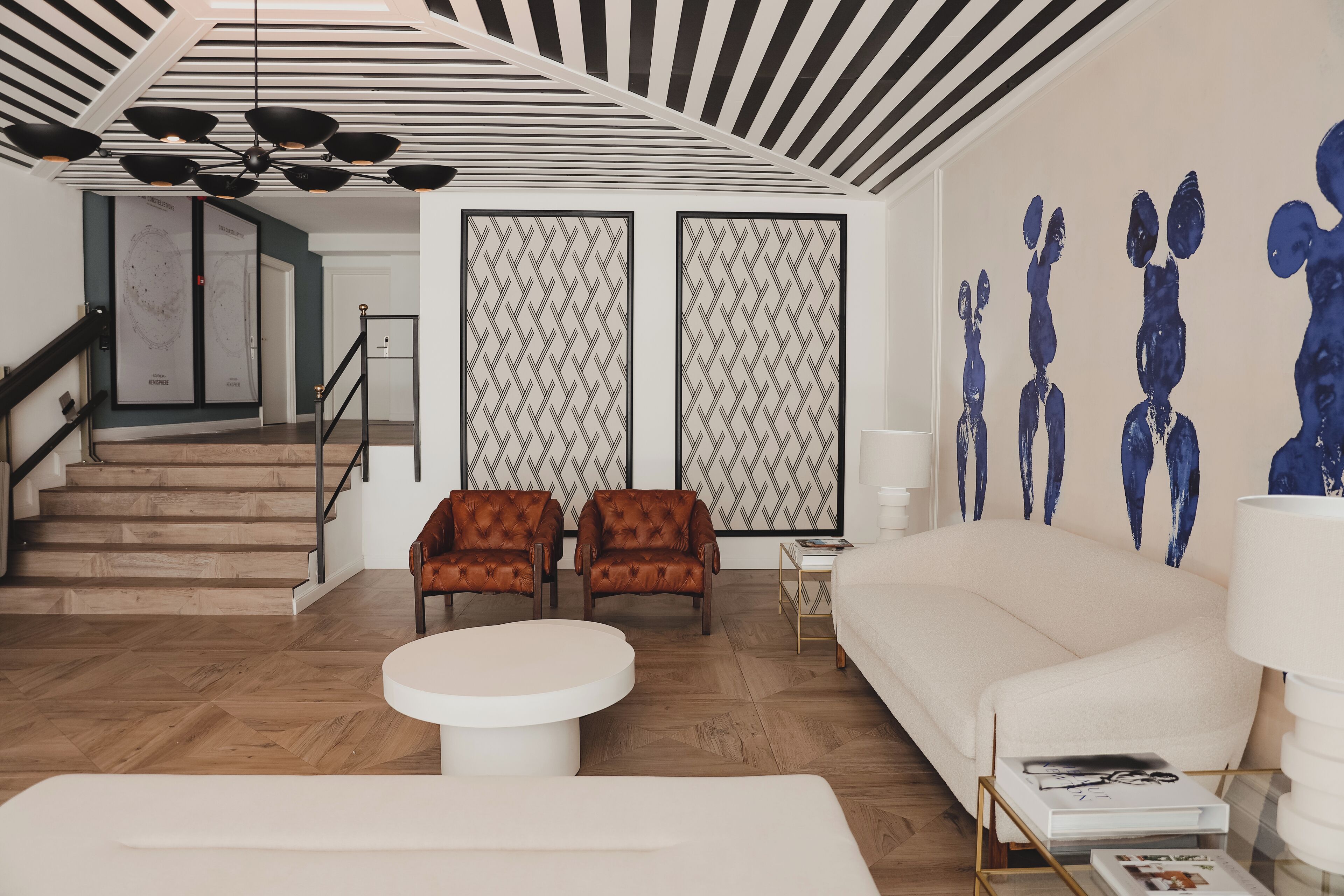 A modern living room with a sofa, two armchairs, a coffee table, and a staircase leading to another room.