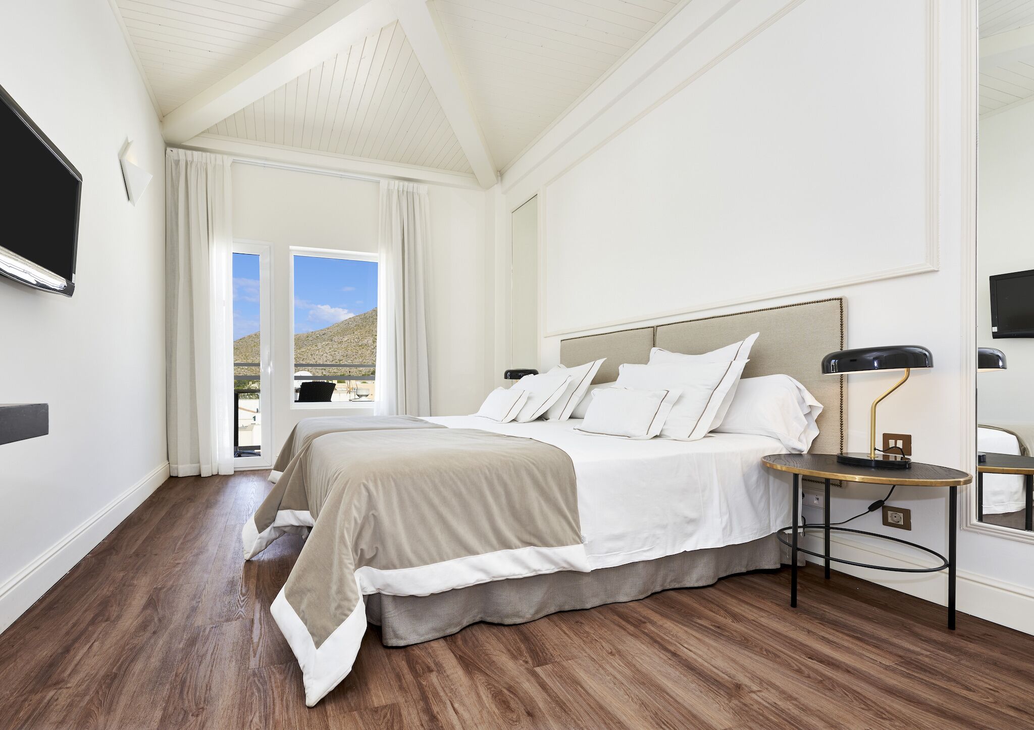 Quarto com cama, mesa de cabeceira, luminária e vista para o exterior.