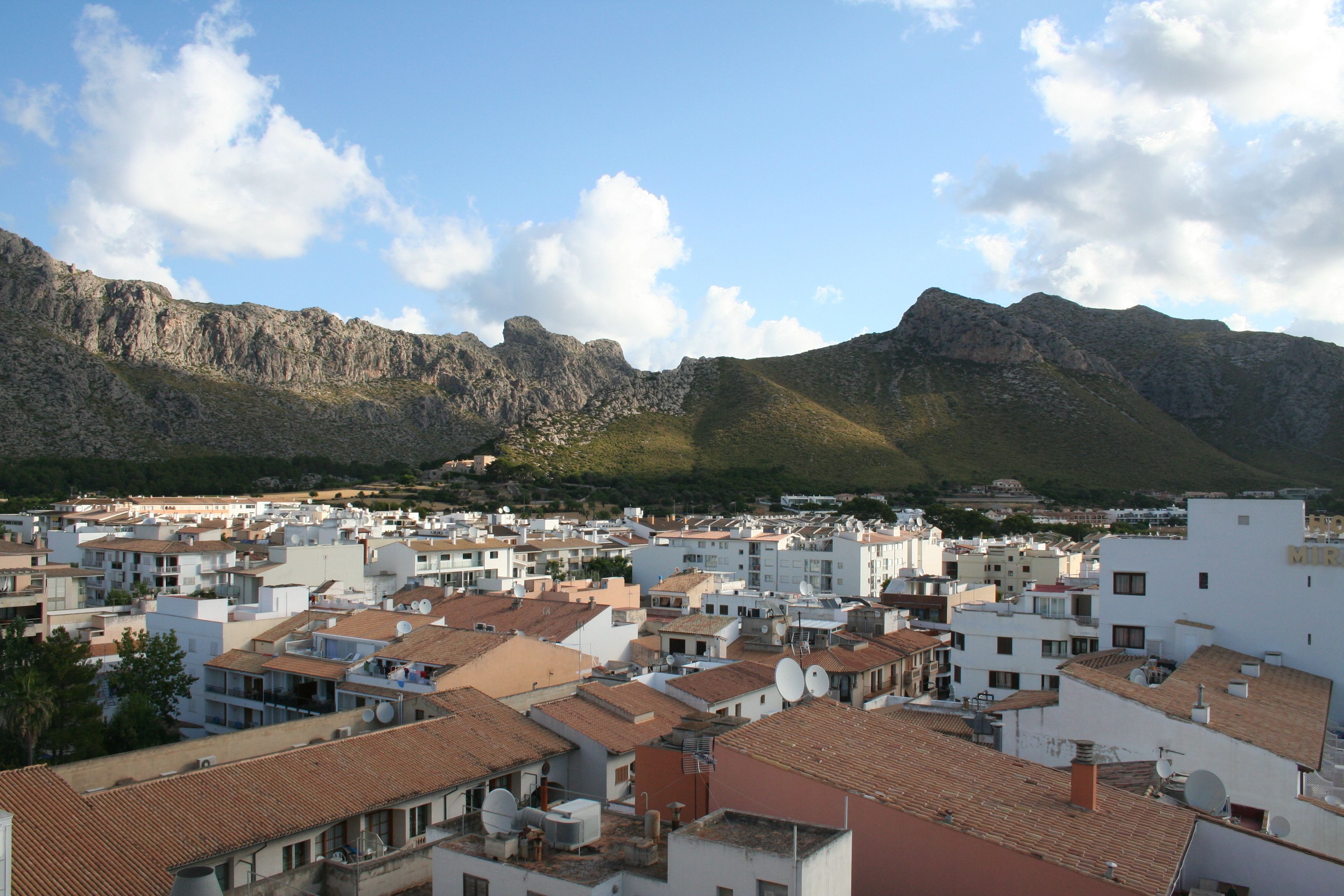 A coastal town with white buildings and red-tiled roofs, surrounded by mountains.